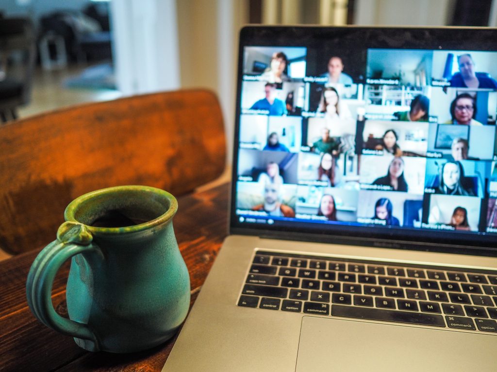 A mug of coffee sits in front of a laptop with a webinar on the screen