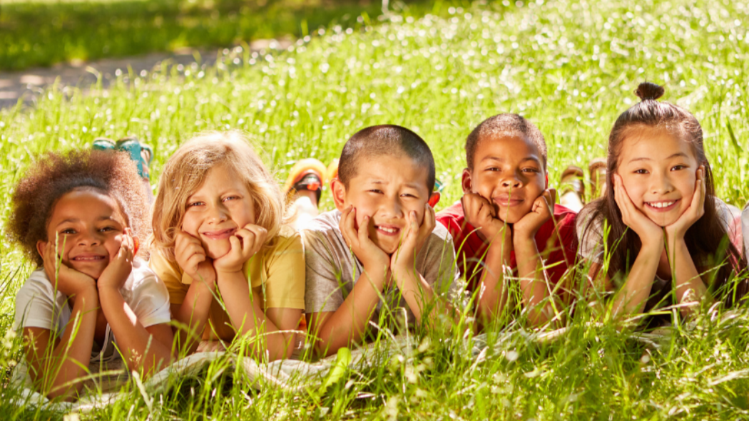 Five kids of different races and genders sit lay on the grass and smile