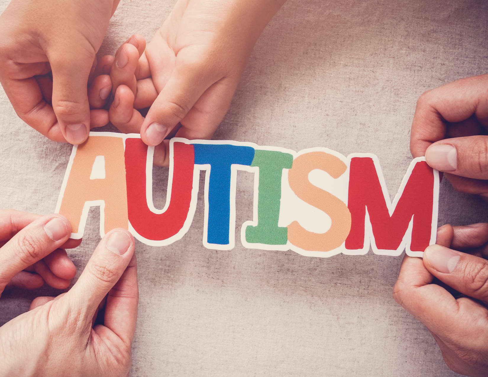 The word Autism is spelled out in colorful letters with three sets of hands helping hold a piece.