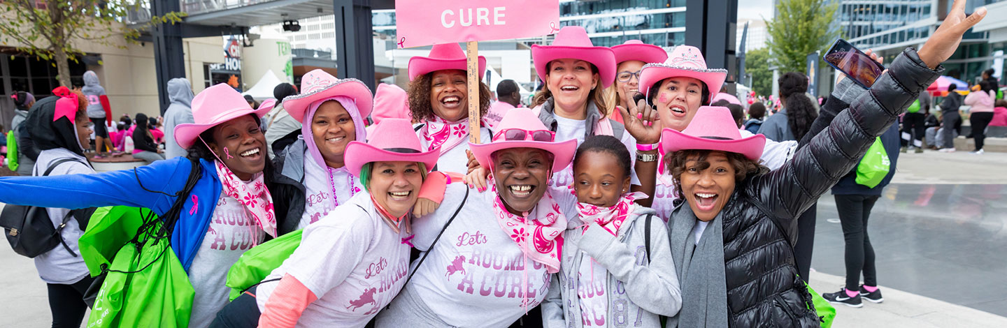 A group of women in pink cowboy hats smile together